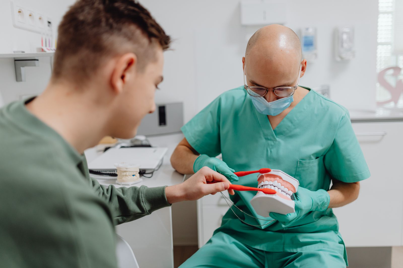 Dentist demonstrating proper brushing technique to a patient using a dental model